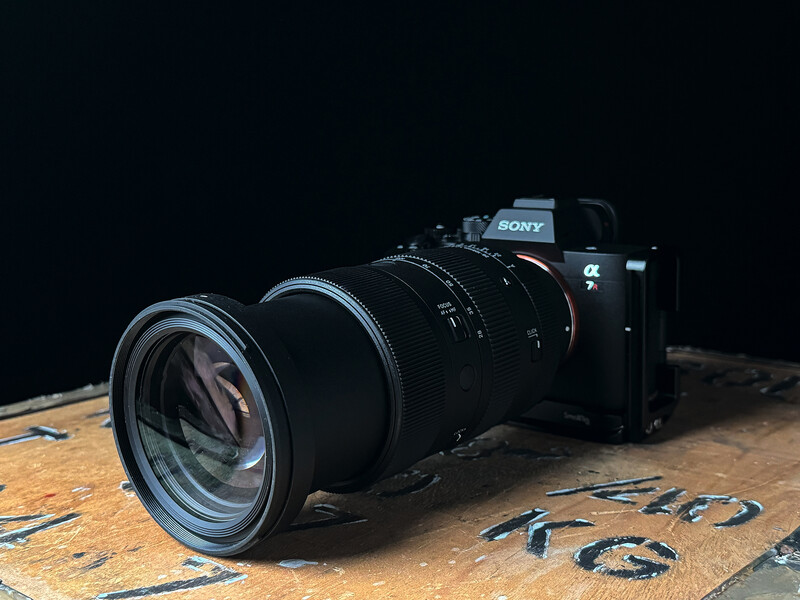 Sony mirrorless camera with large telephoto lens on wooden surface against black background.