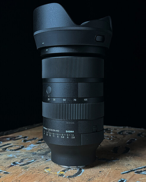 Telephoto zoom lens with hood mounted, positioned vertically against dark background.