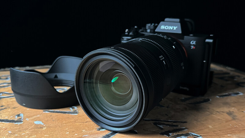 Sony mirrorless camera with attached zoom lens on textured wooden surface against black background.
