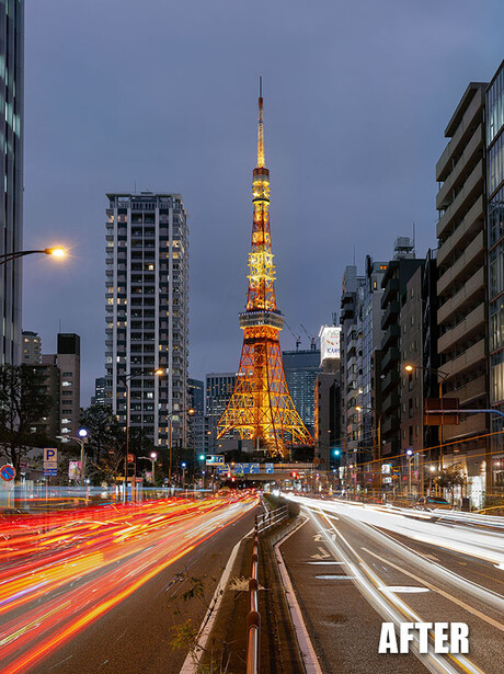 Illuminated pagoda tower at dusk with light trails from traffic in foreground and urban buildings on either side.