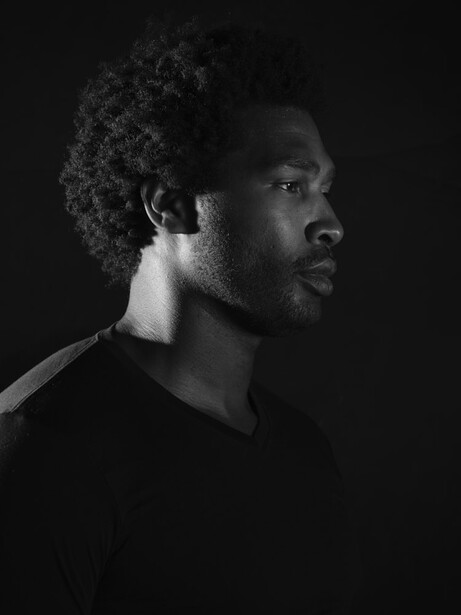 Profile portrait of a man against dark background, lit with dramatic side lighting.