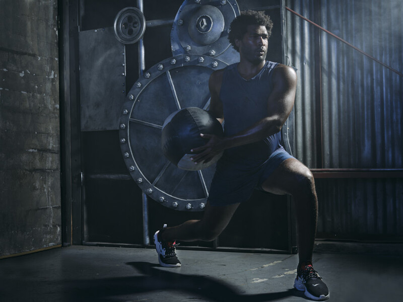 Athlete performing a single-leg squat while holding a large weighted plate in an industrial gym setting.