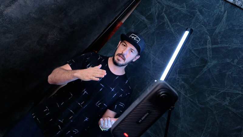 Man holding gaming controller against textured dark wall with neon lighting.