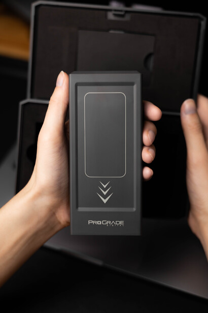 Hands holding a rectangular wireless remote control device with vertical button layout against a dark background.