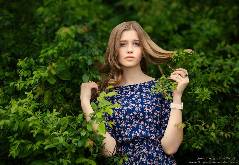 Young woman in navy floral dress posing among lush green foliage.