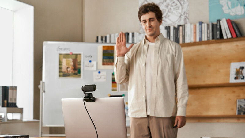 Man waving at laptop camera during video call in home office setting.