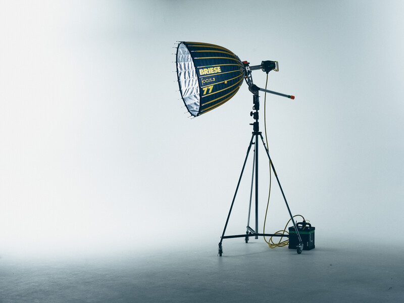 Professional studio light fixture with parabolic reflector mounted on tripod stand with control equipment.