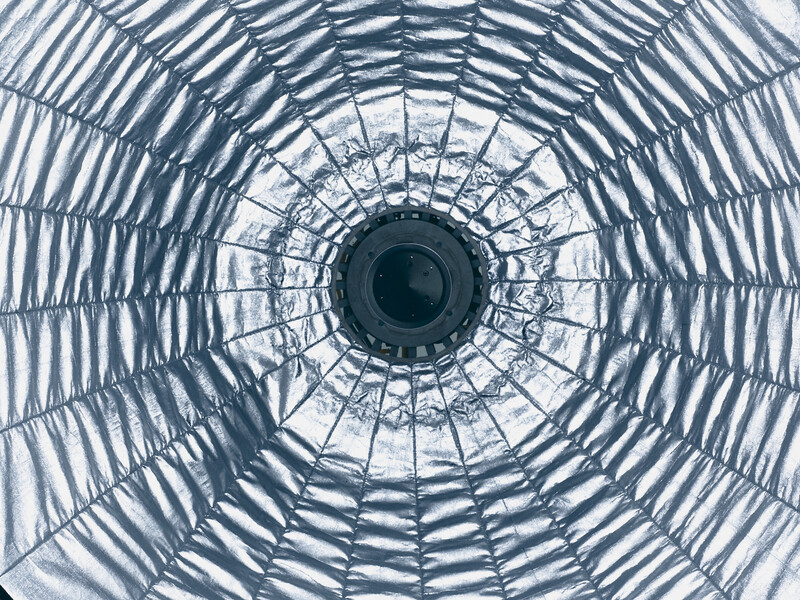 Symmetrical view looking up through a cylindrical metal tunnel or shaft with geometric ribbed structure.
