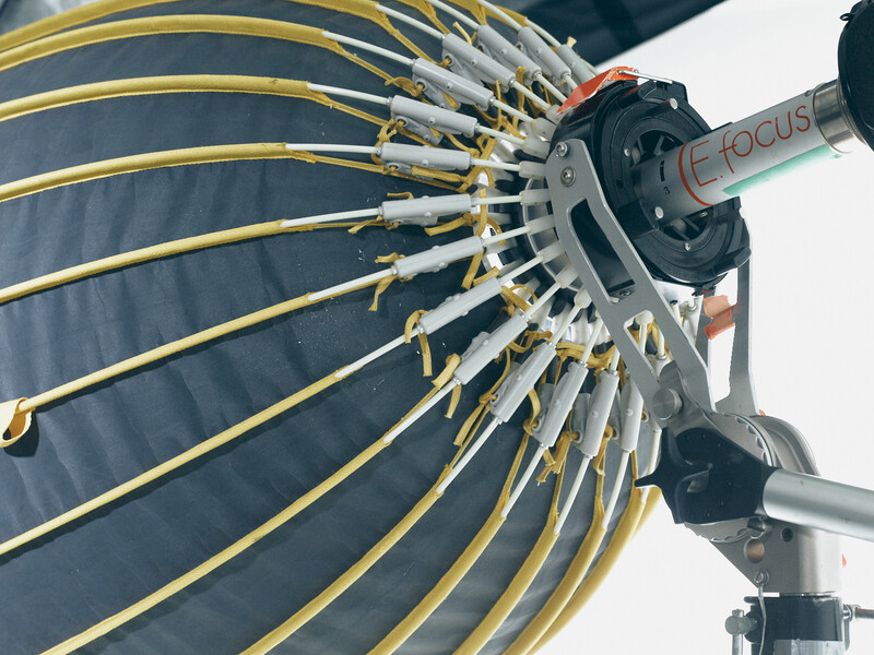 Large parabolic reflector with yellow ribbing and metal framework mounted on a tripod with articulated arm.