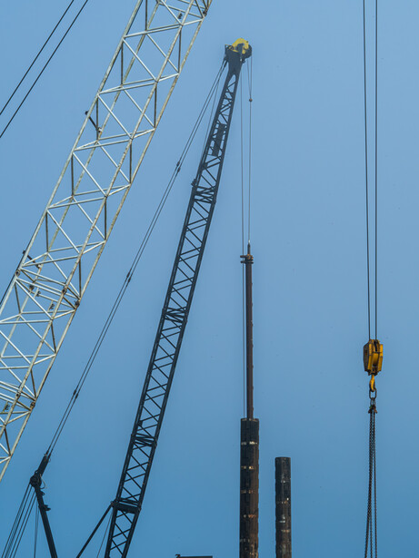 Industrial construction cranes and steel framework against a clear blue sky.