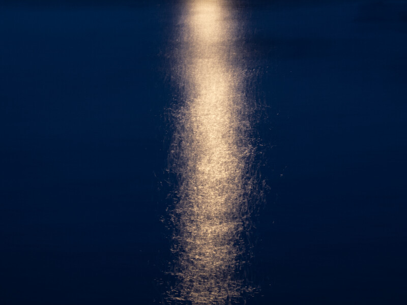 Golden light beam piercing through deep blue water, creating a luminous column against dark surroundings.