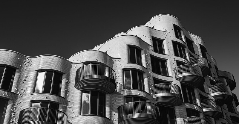 Black and white photograph of a curved modernist building facade with stacked balconies and textured brick walls.