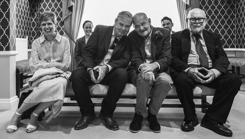 Six people seated on a bench in a black and white portrait photograph.