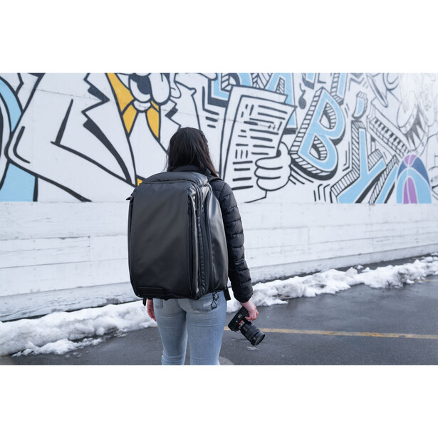 Person wearing black backpack standing before colorful street art mural in winter conditions.