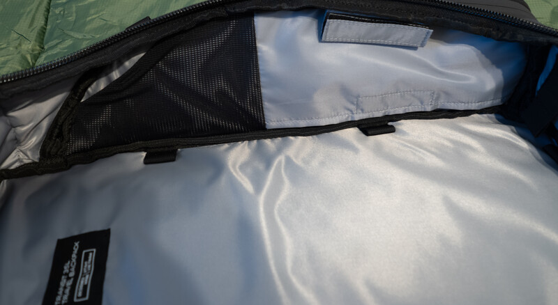 Interior view of a camera bag with white padding and mesh divider panel against bright daylight.