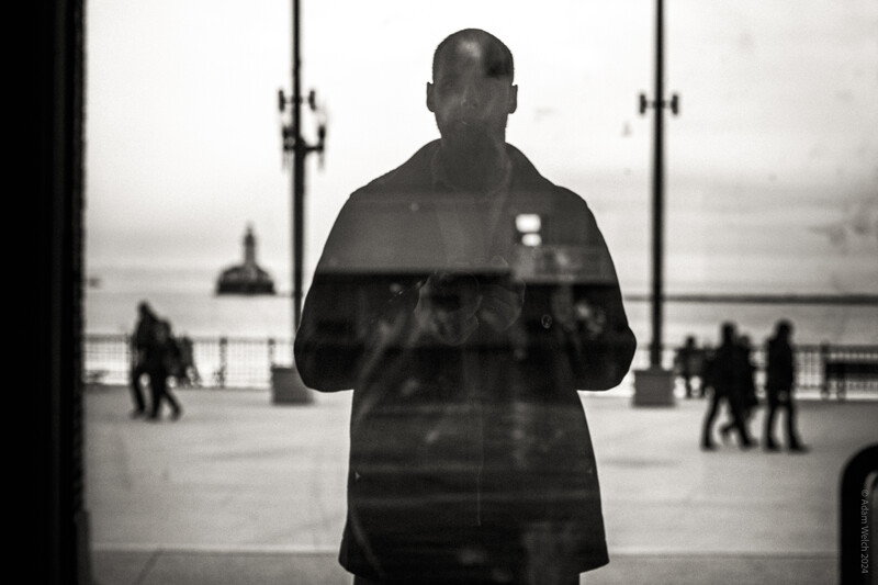 Man standing at a window with double exposure showing an urban waterfront scene behind him.