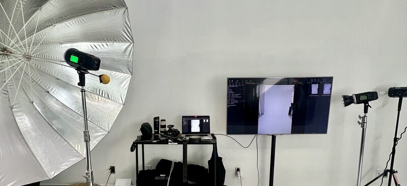 Professional photography studio setup with white umbrella reflector, monitor, and multiple studio lights on stands.
