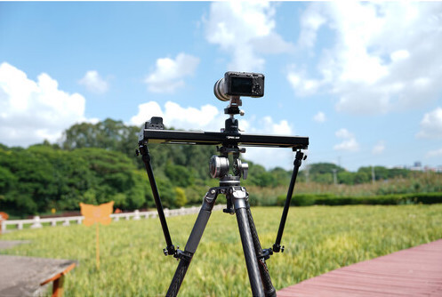 Smartphone mounted on a tripod with articulating arms positioned over a grassy field during daytime.