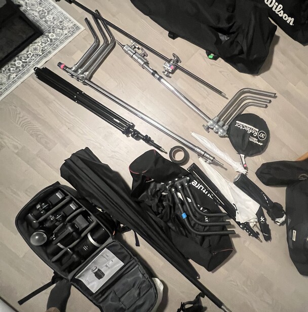 Professional photography and lighting equipment laid out on a white surface, including light stands, softbox, reflector, and gear cases.