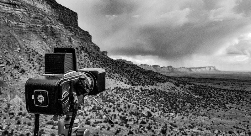 A medium format camera mounted on a tripod overlooking an arid desert landscape with distant plateaus.
