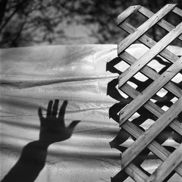 Silhouetted hand reaching upward toward a fire escape on a building wall.