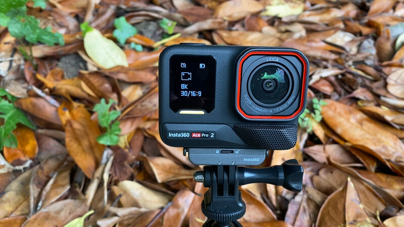 Insta360 Ace Pro 2 action camera mounted on tripod, displayed against autumn leaf litter background.