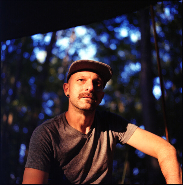 Man wearing a dark t-shirt and cap, posed against a blurred blue bokeh background at night.