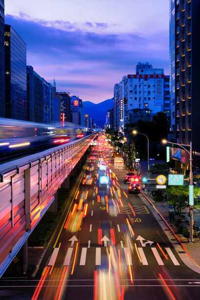 Elevated view of a city street at dusk with light trails from moving vehicles and illuminated buildings.
