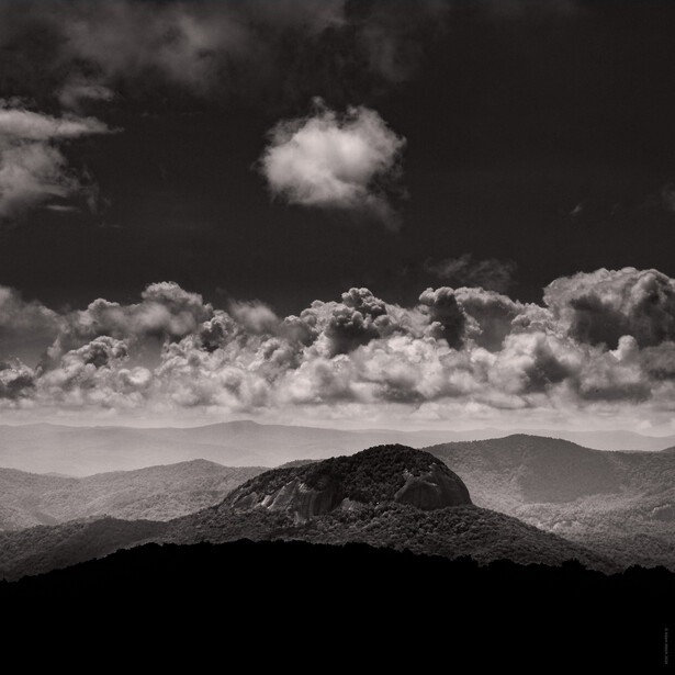 Silhouetted mountain peak against dramatic sky with towering cumulus clouds and distant mountain range.