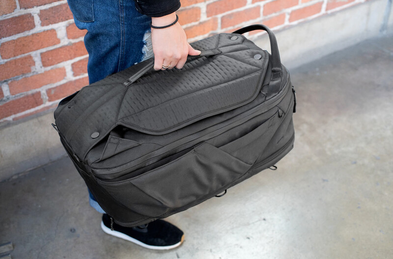 Person holding open a large black camera backpack against a brick wall backdrop.