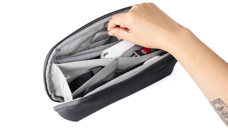 Hand opening a gray camera gear organizer bag displaying multiple internal compartments.