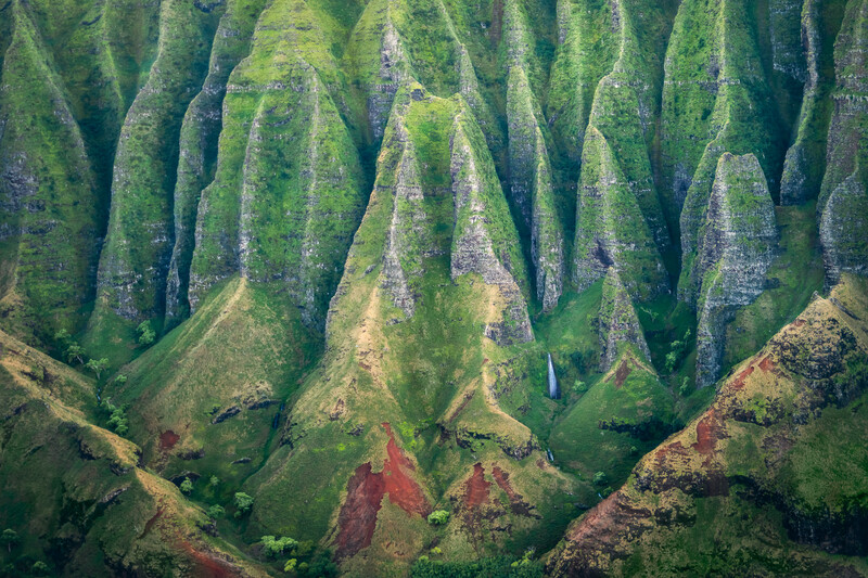 Aerial view of deeply eroded ridges and valleys covered in green vegetation with reddish-brown soil exposed.