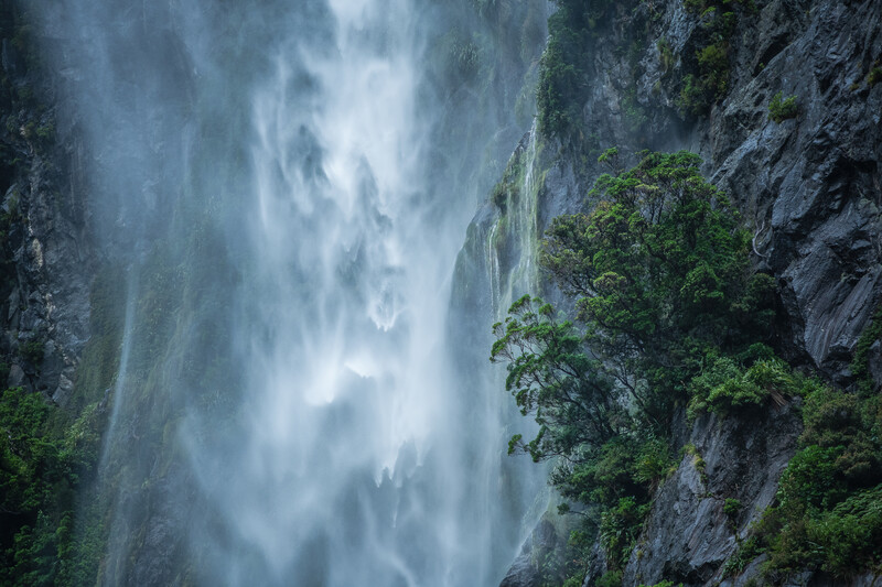 Cascading waterfall flowing down moss-covered rocky cliff face with long exposure blur effect.