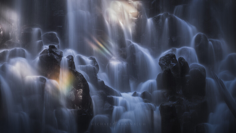 Illustration of silhouetted figures standing among cascading waterfalls with dramatic blue and golden light rays piercing through mist.