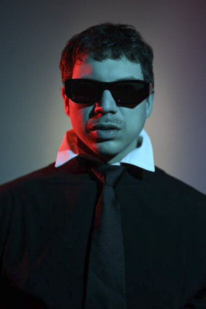 Man wearing dark sunglasses and black jacket against gradient background with red and blue lighting.
