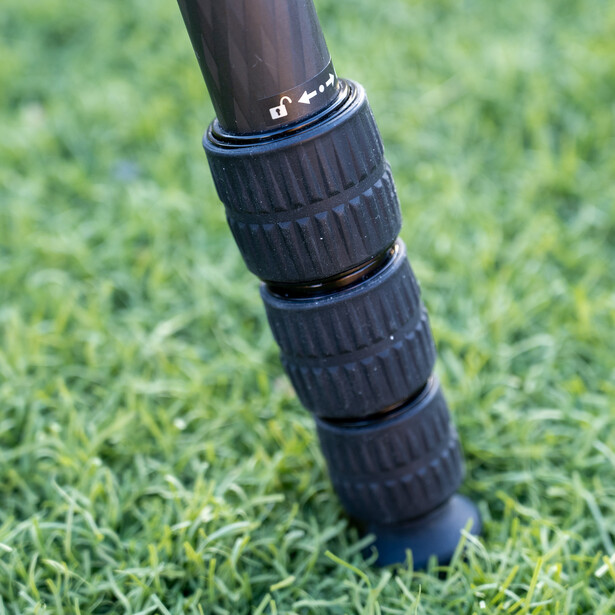 Close-up of a camera lens barrel with focus and zoom rings stacked vertically on grass.