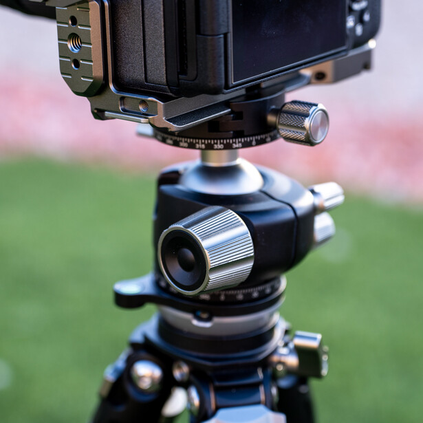 Close-up of a tripod head with ball socket mount and adjustment knobs, supporting professional camera equipment.