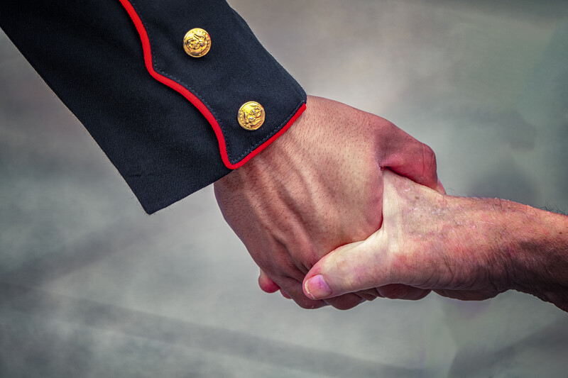 Two people in formal handshake with one wearing navy blazer with gold buttons and red trim.