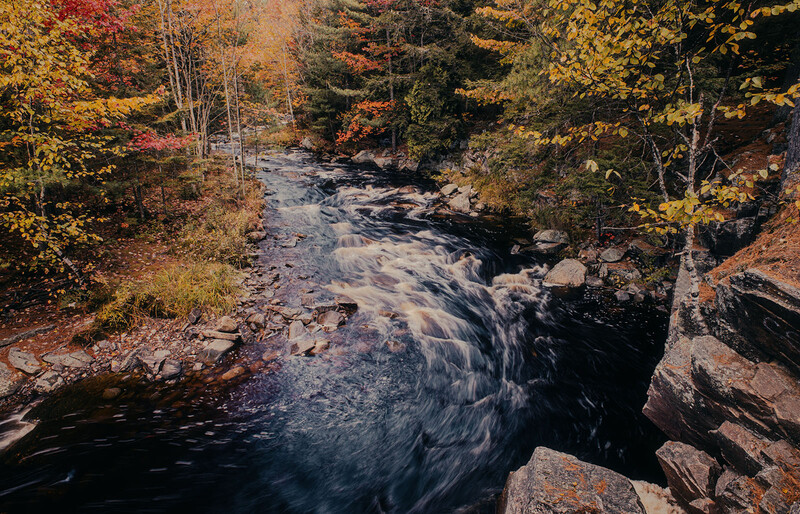 River flowing through autumn forest with golden and red foliage on both banks.