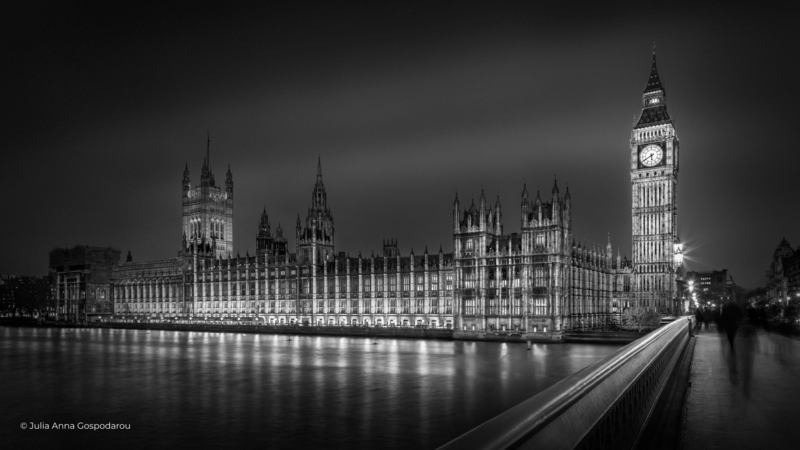 Gothic parliamentary building reflected in still water at night, illuminated by architectural lighting.