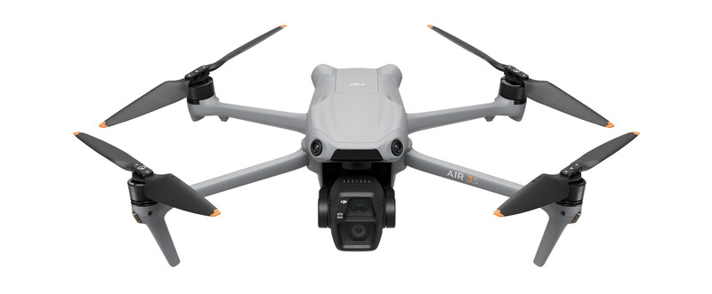 Gray quadcopter drone with four propellers and mounted camera, viewed from above against white background.