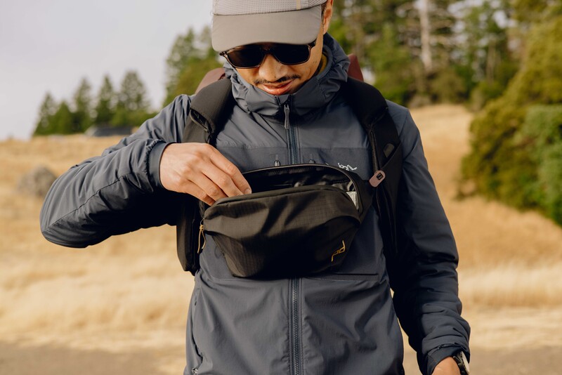 Photographer in winter gear examining a black camera bag in an outdoor mountain setting.