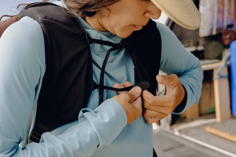 Person adjusting a camera harness or chest strap while wearing a light blue long-sleeve shirt and wide-brimmed hat.