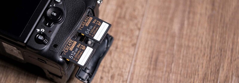 Professional camera body with dual memory card slots containing CompactFlash and SD cards on wooden surface.