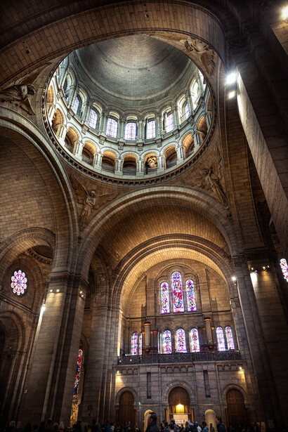 Interior of a grand cathedral with a massive dome, barrel vault ceiling, and ornate arches lit by warm golden light.