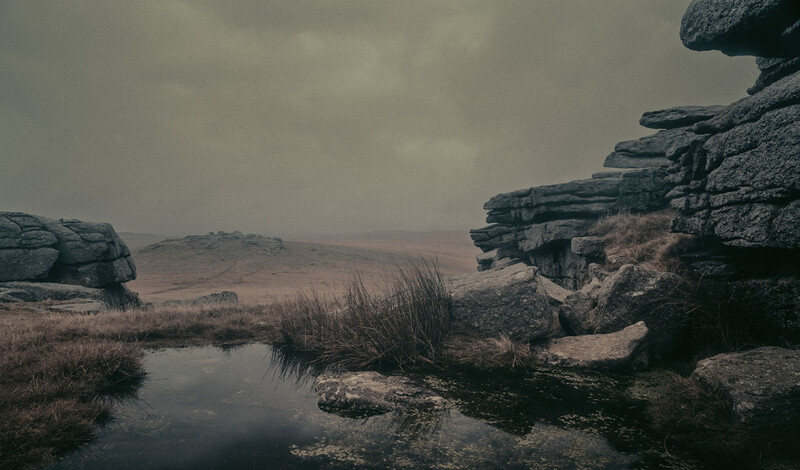 Weathered rock formations reflected in still water beneath an overcast sky.