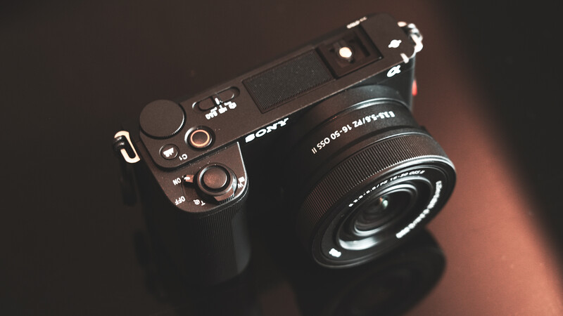 Sony mirrorless camera with attached wide-angle lens on dark surface with warm lighting.