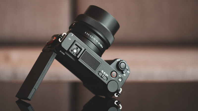 Mirrorless camera with attached lens tilted at an angle against a blurred warm-toned background.