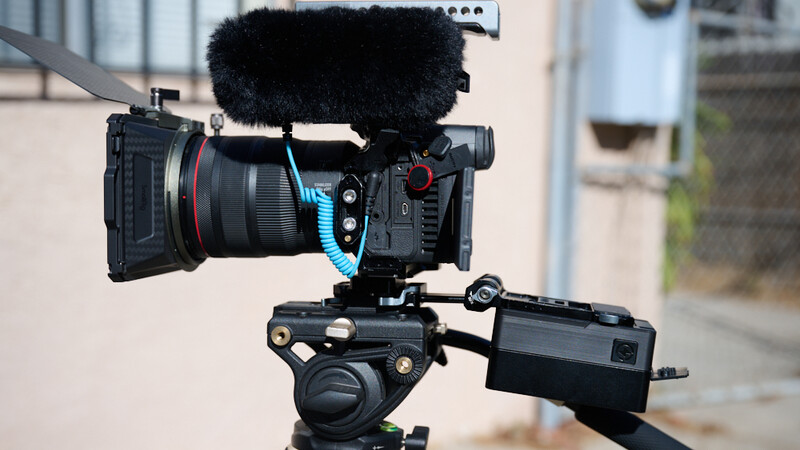 Professional cinema camera mounted on fluid head tripod with microphone and monitor attachments.