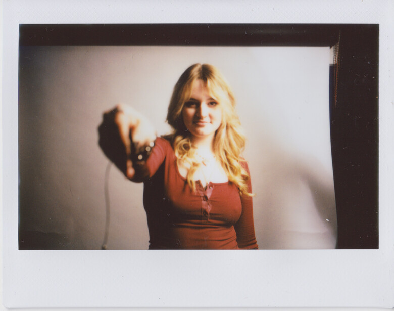 Blonde woman in rust-colored top pointing at camera with warm, directional studio lighting.